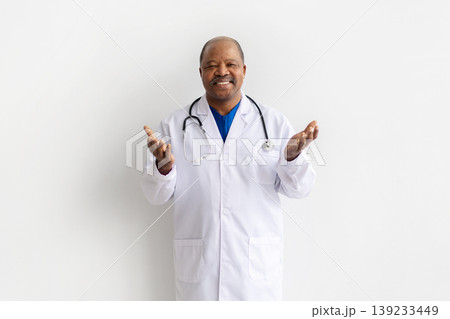 Mature black doctor in white lab coat gesturing with both open hands Mature black doctor in white lab coat gesturing with both open hands 139233449