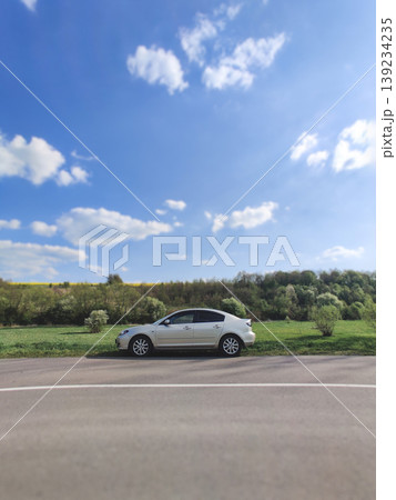 Silver sedan parked on a roadside in a bright spring landscape 139234235