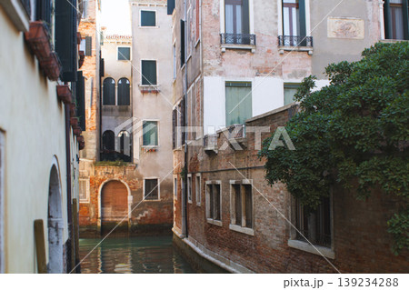 Ancient brick facades of historic Venetian buildings reflected in the calm waters of a narrow canal Ancient brick facades of historic Venetian buildings reflected in the calm waters of a narrow canal 139234288