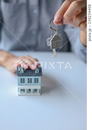 Hand giving key with house-shaped keychain. Concept for buying, selling, renting or leasing a new home. Hand giving key with house-shaped keychain. Concept for buying, selling, renting or leasing a new home. 139234408