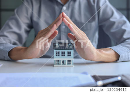 The man's hands sheltering the house model. Concept for home insurance, protection and security The man's hands sheltering the house model. Concept for home insurance, protection and security 139234415