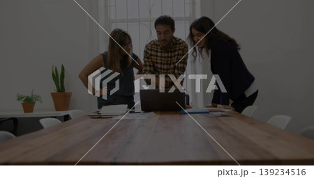 Reviewing documents colleagues in business casual leaning over laptop at meeting table, with pens 139234516