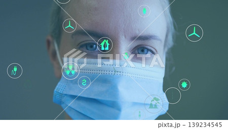 Mid-adult researcher wearing surgical mask analyzing floating energy and eco icons in clinic 139234545