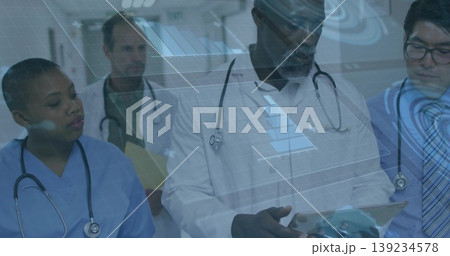 Standing medical team studying tablet with stethoscopes in hospital corridor under digital overlay Standing medical team studying tablet with stethoscopes in hospital corridor under digital overlay 139234578
