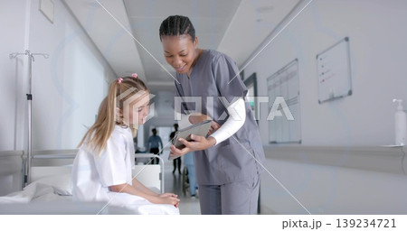 Leaning nurse in scrubs pointing at tablet toward child on bed in corridor, with IV stand Leaning nurse in scrubs pointing at tablet toward child on bed in corridor, with IV stand 139234721