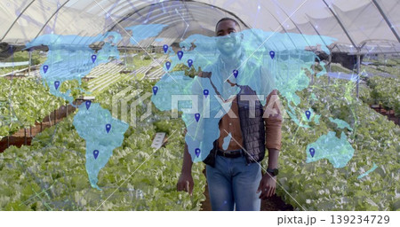 Standing African American man monitoring lettuce in hydroponic greenhouse, with digital world map Standing African American man monitoring lettuce in hydroponic greenhouse, with digital world map 139234729