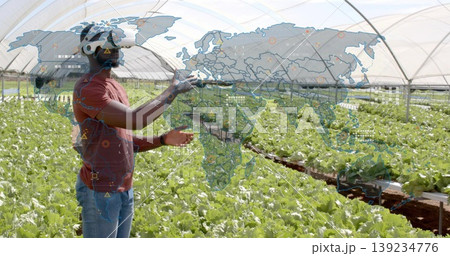 Farmer wearing VR headset holding controllers navigating map in greenhouse, with lettuce trays Farmer wearing VR headset holding controllers navigating map in greenhouse, with lettuce trays 139234776