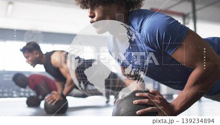 Performing push-up man wearing blue shirt on black medicine ball on rubber gym floor, copy space 139234894