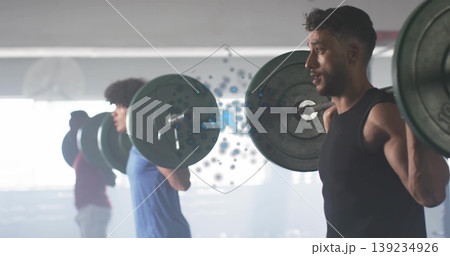 Performing squat male wearing black top, shorts in gym space, barbells and squat racks, copy space Performing squat male wearing black top, shorts in gym space, barbells and squat racks, copy space 139234926