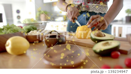 Home cook slicing yellow pepper on wooden cutting board in home kitchen, with avocado and tomatoes 139234947