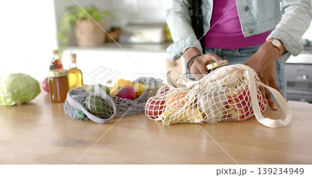Packing woman filling mesh bag with produce in kitchen on wood counter, glass bottles, copy space 139234949