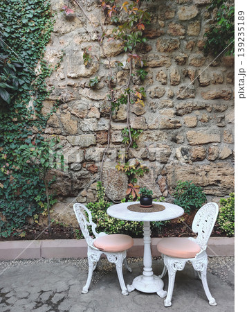 Elegant white vintage table and chairs against an ancient stone wall in Turkey Elegant white vintage table and chairs against an ancient stone wall in Turkey 139235189