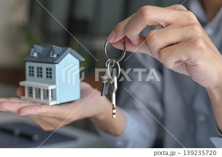 Real estate agent handing over the key with small house model for property purchase or rental. Real estate agent handing over the key with small house model for property purchase or rental. 139235720