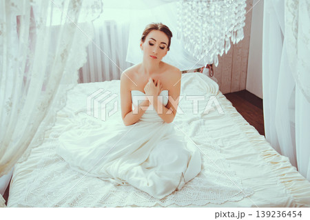 Young girl in white dress sitting on bed with canopy in bright interior 139236454