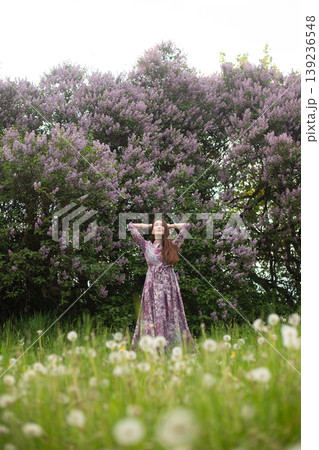 Full length portrait of a woman in a floral dress by lilac bushes Full length portrait of a woman in a floral dress by lilac bushes 139236548