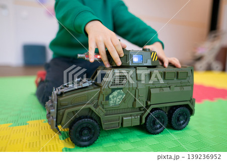 Child playing with a green toy military vehicle on a colorful mat Child playing with a green toy military vehicle on a colorful mat 139236952