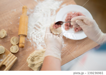 Woman in gloves adding meat filling to dough for handmade dumplings Woman in gloves adding meat filling to dough for handmade dumplings 139236981