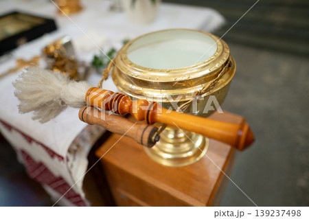 Golden holy water bowl and aspergillum on a church stand Golden holy water bowl and aspergillum on a church stand 139237498