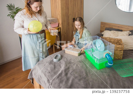 A woman and a girl are preparing a small cage in a well-lit room 139237758