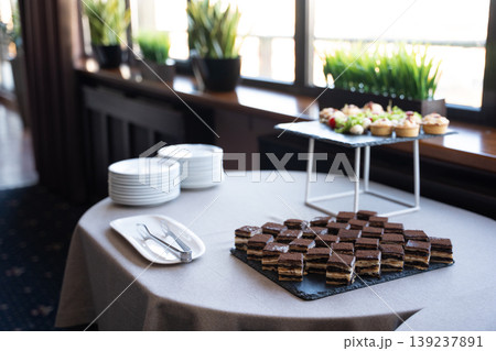 Dessert table with layered chocolate cake squares and assorted appetizers 139237891