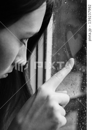 Close-up of a pensive woman drawing a heart on a foggy window Close-up of a pensive woman drawing a heart on a foggy window 139237992