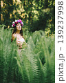 Romantic young woman in flower wreath posing among green fern leaves in summer forest 139237998