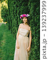 Elegant young woman in flower wreath posing between tall thuja trees in a garden 139237999