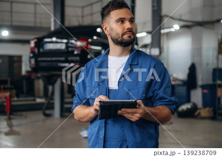 Modern digital tablet is in hands. Male mechanic is working in the car workshop 139238709