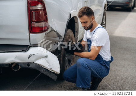 Assesses damage. Mechanic is sitting by the damaged pickup truck outdoors 139238721