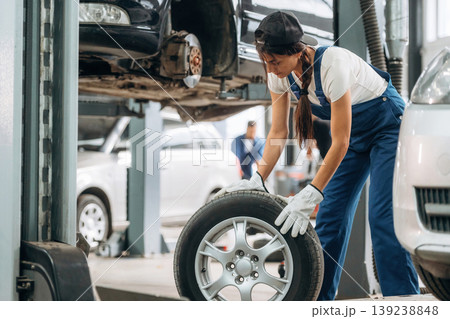 Rolling the wheel. Woman mechanic is with tire in the modern car workshop Rolling the wheel. Woman mechanic is with tire in the modern car workshop 139238848