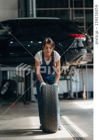 Rolling the wheel. Woman mechanic is with tire in the modern car workshop Rolling the wheel. Woman mechanic is with tire in the modern car workshop 139238859