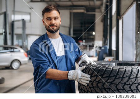 Brand new tire. Male mechanic is working in the modern car workshop 139239003