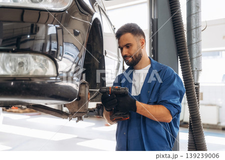 Modern digital tablet is in hands. Male mechanic is working in the car workshop 139239006