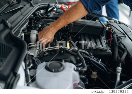 Fixing the car, hood is opened. Close up view of male service station worker at job Fixing the car, hood is opened. Close up view of male service station worker at job 139239332