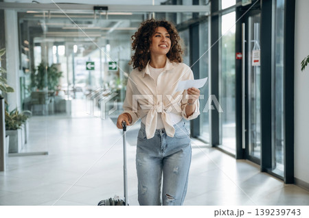Paper document is in hand, pass, ticket. Beautiful woman is in airport hall with suitcase Paper document is in hand, pass, ticket. Beautiful woman is in airport hall with suitcase 139239743