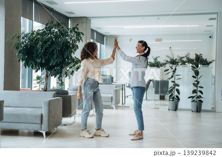 High five hands gesture. Two women are indoors in the modern hall of building at daytime High five hands gesture. Two women are indoors in the modern hall of building at daytime 139239842