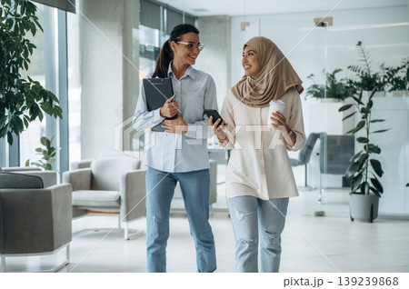 Muslim clothing. Two women are indoors in the modern hall of building at daytime Muslim clothing. Two women are indoors in the modern hall of building at daytime 139239868