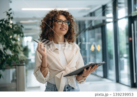 Notepad in hand. Pretty woman in casual clothes is in the modern building indoors 139239953