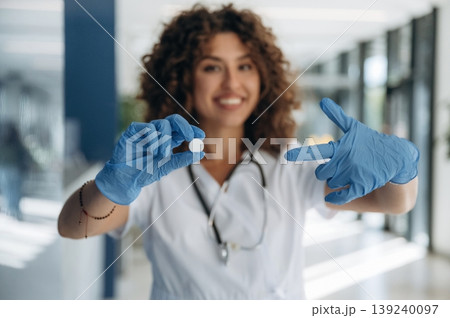 Pill is in hand. Woman doctor is standing indoors in the clinic 139240097