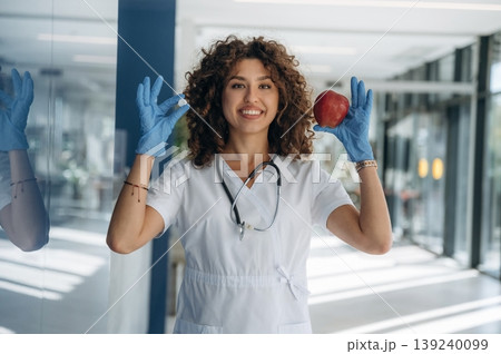 An apple and pill in hands. Woman doctor is standing indoors in the clinic An apple and pill in hands. Woman doctor is standing indoors in the clinic 139240099
