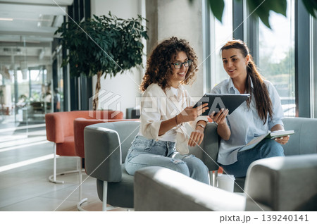 Reading information from the notepad. Two women are indoors in the modern hall of building at daytime 139240141