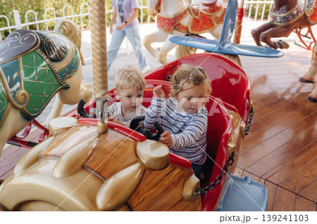 A girl and a boy ride on a carousel, in a car. Happy kids A girl and a boy ride on a carousel, in a car. Happy kids 139241103