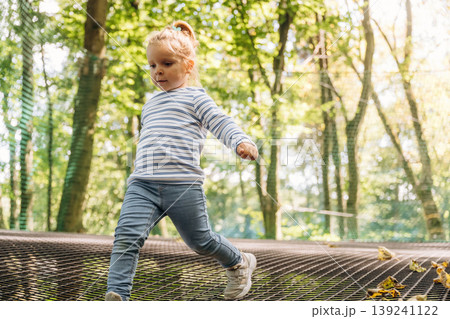 Wellness conception. Little girl is playing on the children's amusement ropes course Wellness conception. Little girl is playing on the children's amusement ropes course 139241122