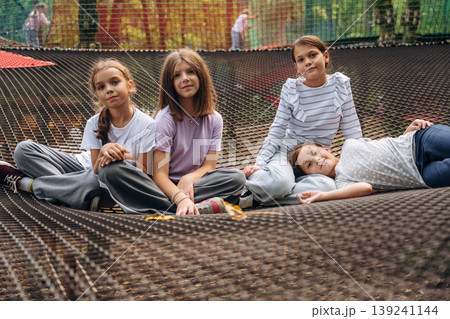 In casual clothes, relaxed, sitting. Kids are playing on the children's amusement ropes course In casual clothes, relaxed, sitting. Kids are playing on the children's amusement ropes course 139241144