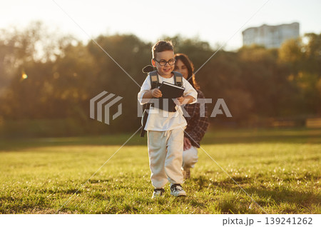 Pupil is with book and backpack. Mother and son together in an open field during daytime 139241262