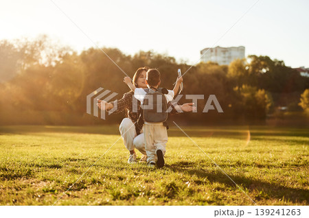 Pupil is with book and backpack. Mother and son together in an open field during daytime 139241263