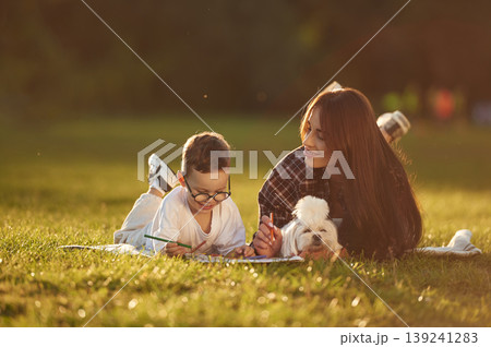 Relaxed, on the blanket, with little cute dog. Mother and son together in an open field during daytime 139241283