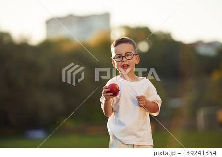Fresh apple is in hand, healthy eating. Boy is having fun on the field under sunlight at daytime Fresh apple is in hand, healthy eating. Boy is having fun on the field under sunlight at daytime 139241354