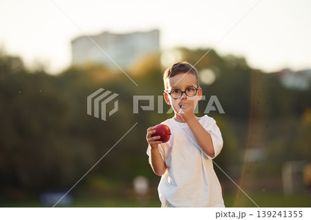 Fresh apple is in hand, healthy eating. Boy is having fun on the field under sunlight at daytime Fresh apple is in hand, healthy eating. Boy is having fun on the field under sunlight at daytime 139241355
