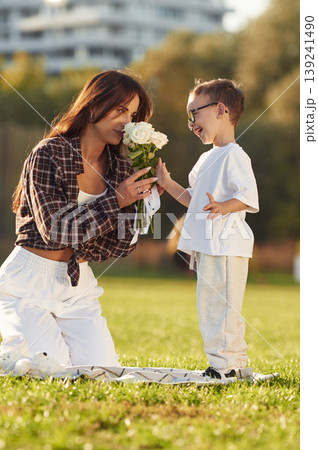 Gives flowers to woman, gift conception. Mother and son together in an open field during daytime Gives flowers to woman, gift conception. Mother and son together in an open field during daytime 139241490